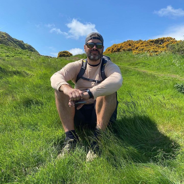 Will Stojcic, founder of Traviis, sitting on a grassy hillside in Scotland